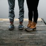 Two pairs of feet standing on the dock of a river.